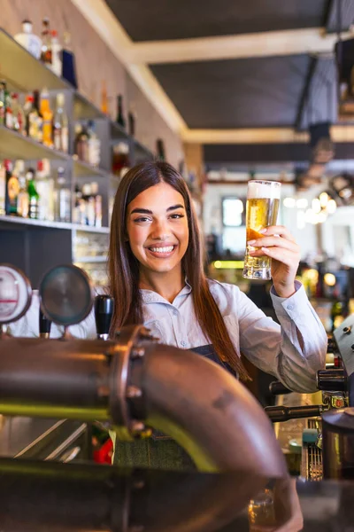 Beautiful smiling female Bartender serving a draft beer at the bar counter , Young woman serving draft beer. Smiling female bartender pouring from tap fresh beer into the glass in pub.