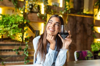 Image of cute pretty young woman sitting in cafe holding glass and drinking wine. portrait of a beautiful wine tasting tourist woman.