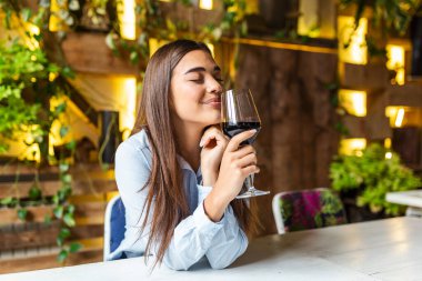 Beautiful woman tasting wine while sitting in restaurant. Image of cute pretty young woman sitting in cafe holding glass and drinking wine. portrait of a beautiful wine tasting tourist woman.