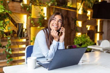 Young business woman using her laptop at a cafe. Beautiful woman sitting at a table with a cup of coffee and mobile phone surfing the net on her laptop computer.