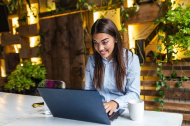 Young businesswoman drinking coffee and using tablet laptop in cafe. Attractive Caucasian elegant brunette sitting in cafe, enjoying coffee. Laptop is on the table.