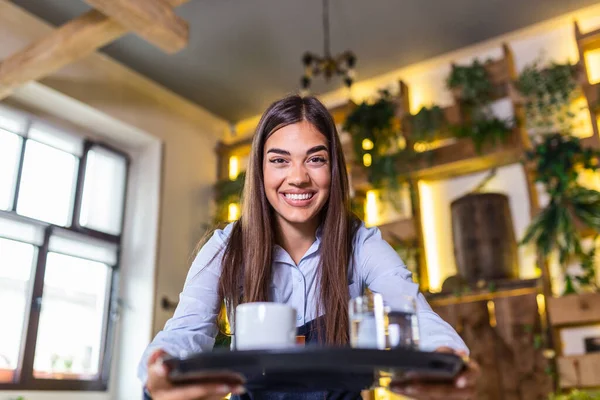 Happy waitress holding tray with cup of coffee, working in cafeteria and serves the table