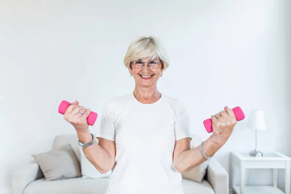 Senior woman exercising with dumbbells at home. Sporty beautiful woman exercising at home to stay fit. Elderly woman exercising at home in a living room. Fitness, workout, healthy living and diet concept.