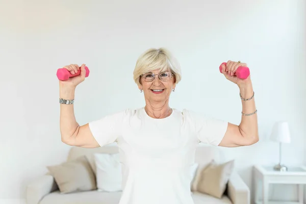 Senior woman exercising with dumbbells at home. Sporty beautiful woman exercising at home to stay fit. Elderly woman exercising at home in a living room. Fitness, workout, healthy living and diet concept.