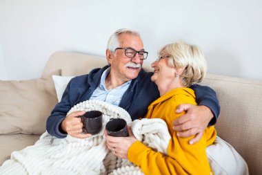 Happy old couple sitting on the sofa. Feeling cozy,drinking coffee or tea