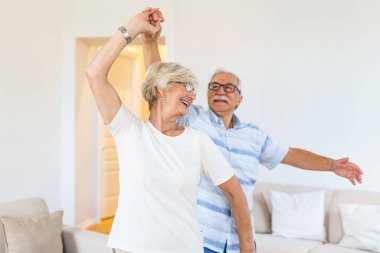 Kaygısız mutlu aktif yaşlı yaşlı çift oturma odasında gülerek atlama dans, olgun orta yaşlı eşi elini tutarak neşeli emekli yaşlı koca evde eğlenceli eğlence emeklilik yaşam tarzı zevk