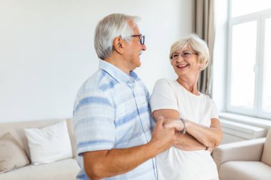 Senior couple relaxing at home, dancing. Elderly couple are enjoying a dance in the living room of their home.