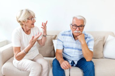 Angry elderly woman arguing with her husband. Senior couple having difficulty in marriage. Old couple sitting on the sofa at home