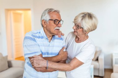 Unhappy senior man suffering from elbow pain at home. His wife taking care of him