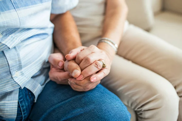 Close up of mature old husband and wife hold hands show love and care. Senior couple holding hands while sitting together at home. Elderly relationships, marriage concept
