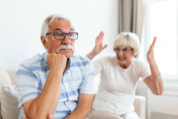 Senior couple arguing. Elderly woman frustrated with her husband. Older couple sitting on the sofa at home,having fight. Marriage issues, pre-divorce period