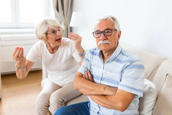 Angry elderly woman arguing with her husband. Senior couple having difficulty in marriage. Old couple sitting on the sofa at home