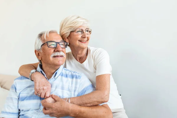 Portrait loving older wife hugging husband sitting on cozy couch. Happy senior mature couple smilling and looking at camera, posing for family photo at home. Elderly couple feeling happy