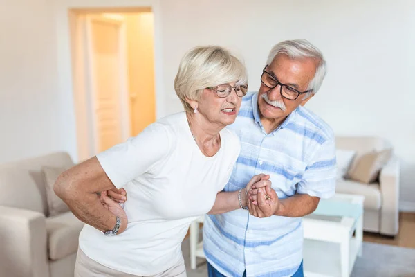 Senior couple at home. Handsome old woman is having back pain and her attractive old husband supports her.