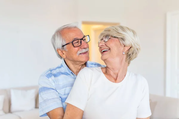 Elderly couple standing in the living room. Portrait of happy senior couple embracing each other in living room at home. Old couple looking each other with love and smilling.