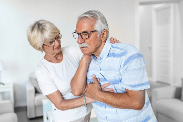 Senior man with neck pain and concerned elderly woman at home