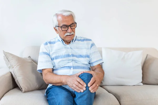 Elderly Man Sitting Sofa Home Touching His Painful Knee People — Stockfoto