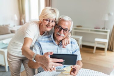 Elderly spouses at home. Wife hugs husband.Having pleasant conversation chatting on video call with grown up children and grandchildren using tablet