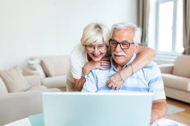 Elderly spouses at home. Wife hugs husband.Having pleasant conversation chatting with grown up children and grandchildren using wireless tech concept