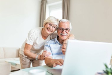 Elderly spouses at home. Wife hugs husband.Having pleasant conversation chatting with grown up children and grandchildren using wireless tech concept