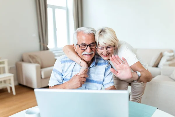 Happy old family couple talking with grandchildren using laptop , surprised excited senior woman looking at computer waving and smiling.