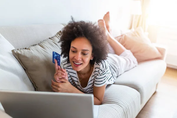 Internet payment. Happy cheerful woman looking at the Internet screen while making an Internet payment. Happy young woman with credit card and laptop sitting on sofa at home. Online payment