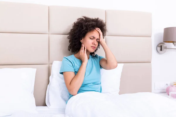 Portrait of an attractive woman sitting on a sofa at home with a headache, feeling pain and with an expression of being unwell. Upset depressed woman lying on couch feeling strong headache migraine.