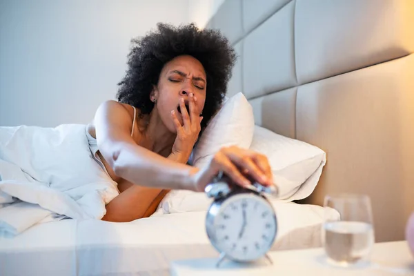 Young black woman yawn awakening tired insomnia holding alarm clock. wake up early in morning. Girl stop snooze alarm. female waking up sleepy and tired. woman wake up with alarm clock snooze concept.