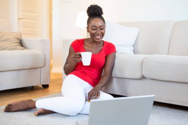 Young woman having online video chat with friends via laptop with coffee cup in hand, surprised expression, Woman can't believe talking with family on video call