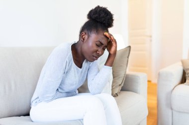 African American Woman in painful expression holding hands against belly suffering menstrual period pain, lying sad on home bed, having tummy cramp in female health concept