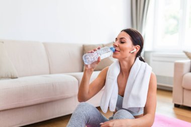 Genç yetişkin kadın plastik şişeden su içme, fitness mat üzerinde oturan ve evde eğitim den sonra dinlenme