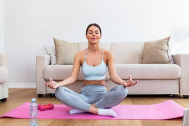 Self learning. Woman using laptop to training yoga online in living room. Girl does yoga training exercises on a mat in her living room. She follows an online exercise course video on her laptop.