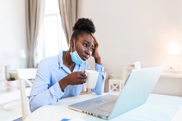I can not believe I caught a cold! Frustrated african american businesswoman drinking hot beverage with protective mask. It\'s flu season. Sick young business woman at work