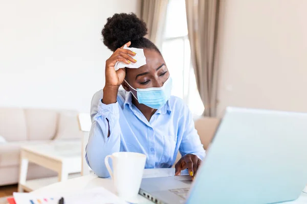 Woman sitting alone in her office and coughing as she suffers from a cold. Medical mask and hand disinfectant and stressed woman. Shot of a businesswoman working in her office while she is sick.