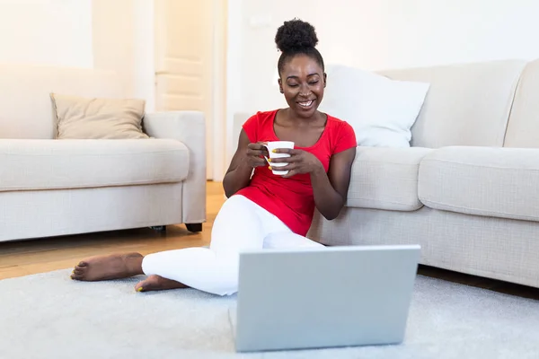 Young woman having online video chat with friends via laptop with coffee cup in hand, surprised expression, Woman can\'t believe talking with family on video call