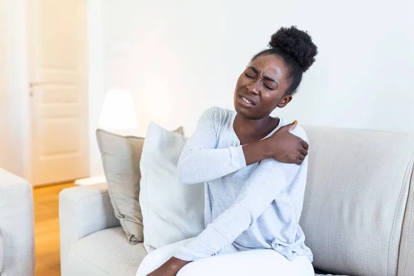 African Woman Sitting Couch Take Break Touches Her Shoulder Suffers — Stock Photo, Image
