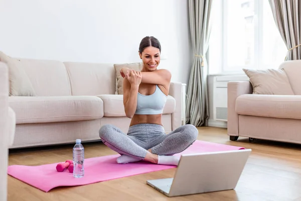 Girl training at home, doing workout and watching videos on laptop, training in living room. She is watching video on the internet and repeating the tasks
