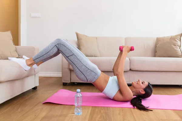 Young woman is exercising with dumbbells at home. Fitness, workout, healthy living and diet concept. Young woman doing gymnastic exercises at home. Determined woman losing weight at home and exercising with dumbbells