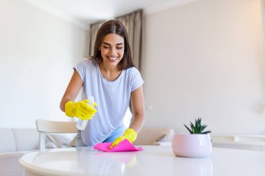 Woman wearing yellow rubber protective gloves and cleaning white table. Happy Female Housekeeper Cleaning the house