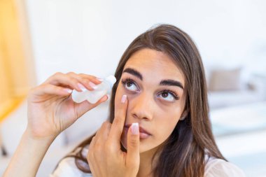 Photo of a woman using eye drop. Female dropping eye lubricant to treat dry eye or allergy. Sick girl treating eyeball irritation or inflammation; sick woman suffering from irritated eye, optical symptoms.