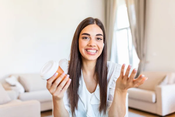 Excited young woman looking at camera, holding funny conversation with colleagues online, webcam view. Head shot of young woman with headphones laughing, having fun from home office.