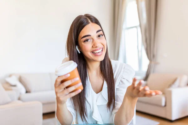 Excited young woman looking at camera, holding funny conversation with colleagues online, webcam view. Head shot of young woman with headphones laughing, having fun from home office.