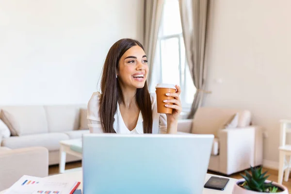 Happy young woman in headphones speaking looking at laptop making notes, girl student talking by video conference call, female teacher trainer tutoring by webcam, online training, e-coaching concept, drinking coffee or tea