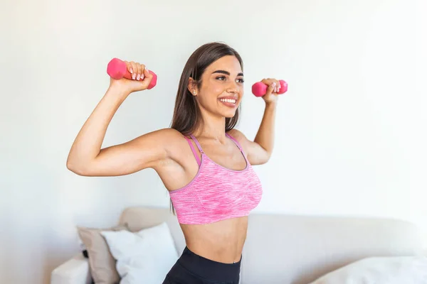 Sporty woman exercising with dumbbells at home. Photo of active woman in sportswear working out. Dynamic movement. Side view. Sport and healthy lifestyle