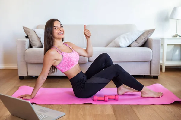 Young woman exercising at home in a living room. Video lesson. Young woman repeating exercises while watching online workout session. Beautiful young woman doing fitness exercise at home