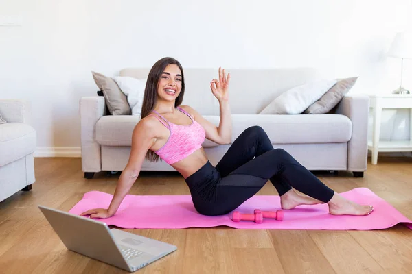 Young woman exercising at home in a living room. Video lesson. Young woman repeating exercises while watching online workout session. Beautiful young woman doing fitness exercise at home