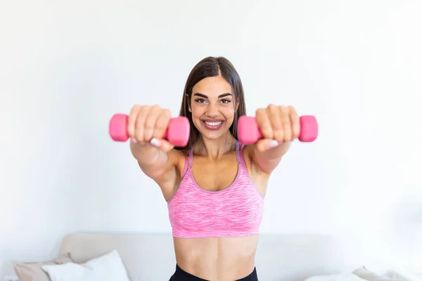 Woman exercising with dumbbells at home. Sporty beautiful woman exercising at home to stay fit. Young woman exercising at home in a living room. Fitness, workout, healthy living and diet concept.