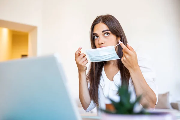 Businesswoman putting on protective mask working on laptop in the office. Focused company employee worker in protective facial mask working on laptop at home keeping covid 19 virus quarantine measures