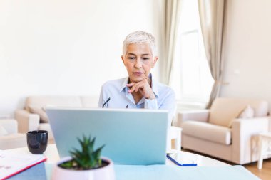 Portrait of casual woman using her laptop while sitting home office and working. An attractive middle aged businesswoman sitting in front of laptop and managing her small business from home.