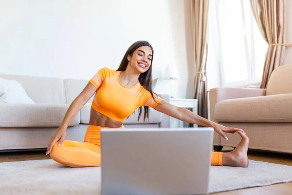 Girl training at home, doing workout and watching videos on laptop, training in living room. Beautiful woman is doing side plank exercise. She is watching video on the internet and repeating the tasks